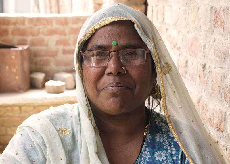 A senior woman, wearing eyeglasses, smiles at the camera