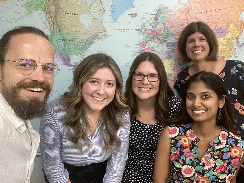 Photo of a group of people as they pose for the camera in front of a world map.