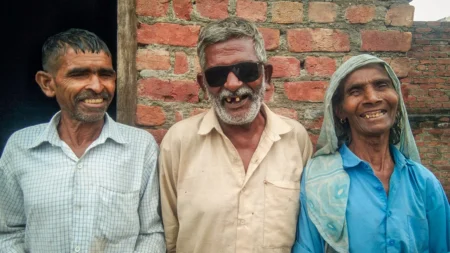 Harprasad beams from between two family members, wearing heavy sunglasses to protect his eyes after his cataract surgery.
