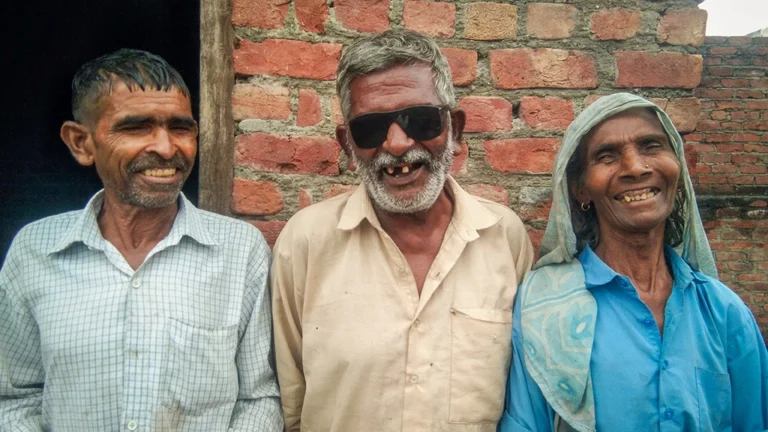 Harprasad beams from between two family members, wearing heavy sunglasses to protect his eyes after his cataract surgery.