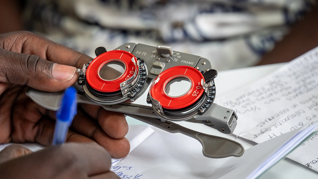 Optical frames used for refraction are held in a man's left hand while the right hand jots down notes.