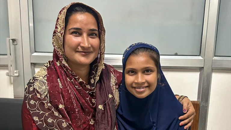 A woman and girl sit close together, smiling.