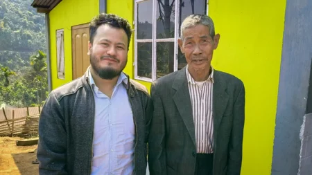 Robiroy poses with a man outside of a yellow house.