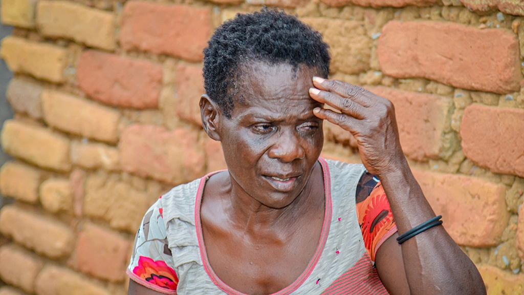 A woman with short hair points to her forehead above her left eye. 